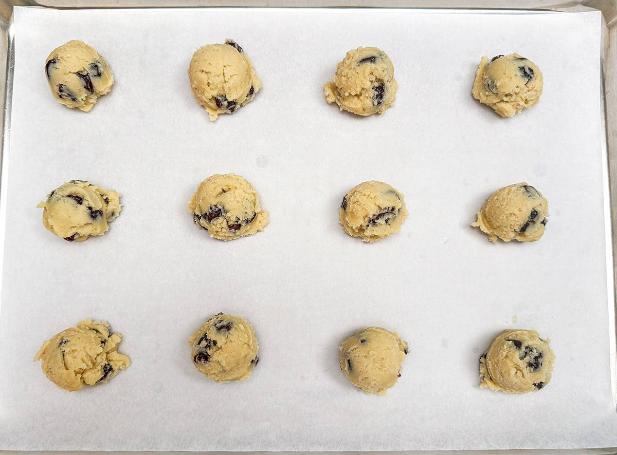 Twelve scooped cookie dough placed on a parchment-lined cookie sheet pan.