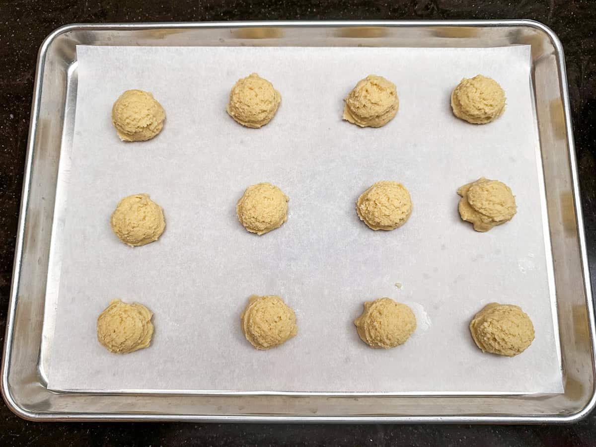 Scooped cookie dough on a parchment paper lined sheet pan.