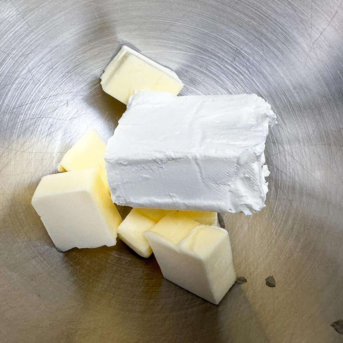 Cubed butter and a block of cream cheese getting ready to be blended in a mixer bowl.