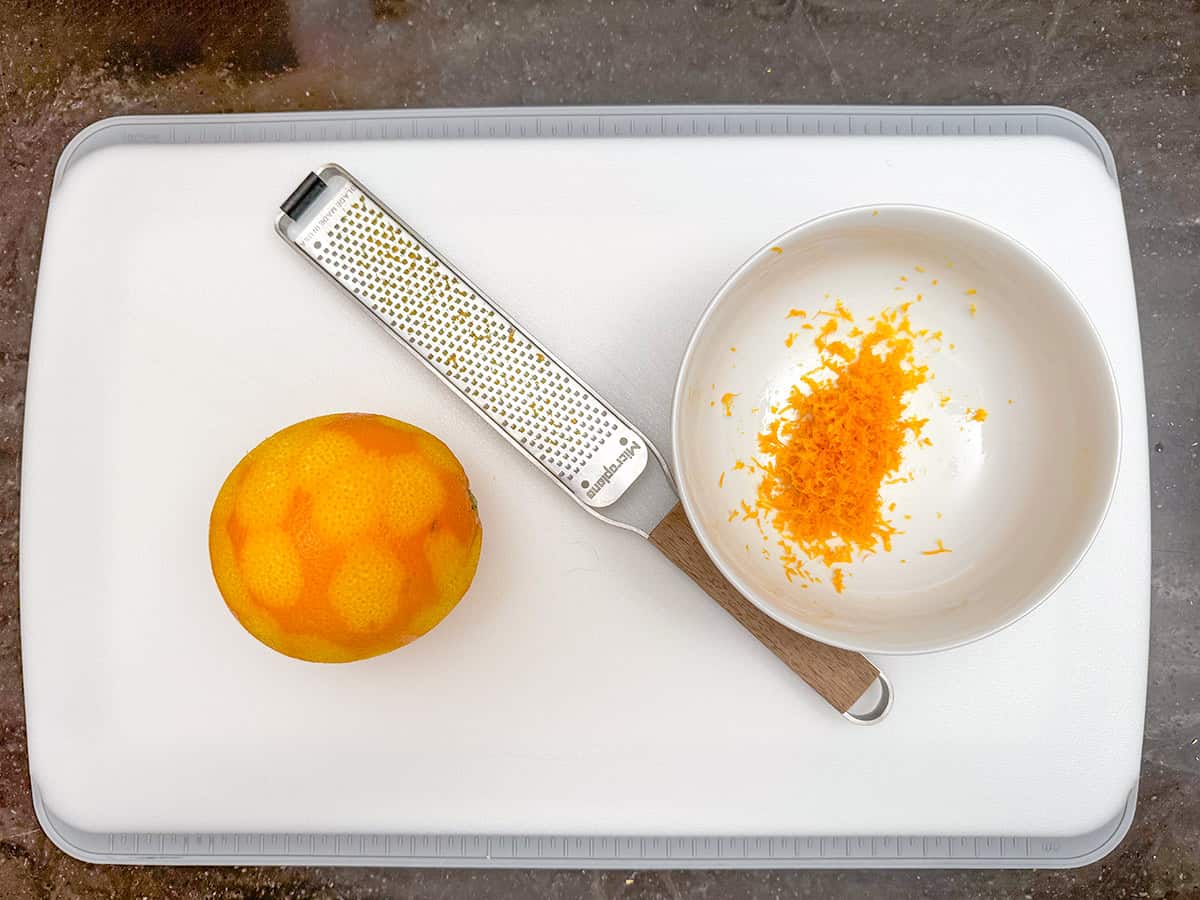 Orange zest in a bowl along side a zester. Showing how deep to zest an orange.