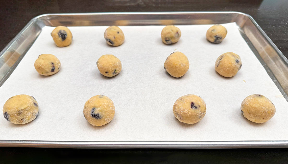 Cookie dough balls that have been rolled in fine sugar and sitting on a parchment-lined sheet pan.