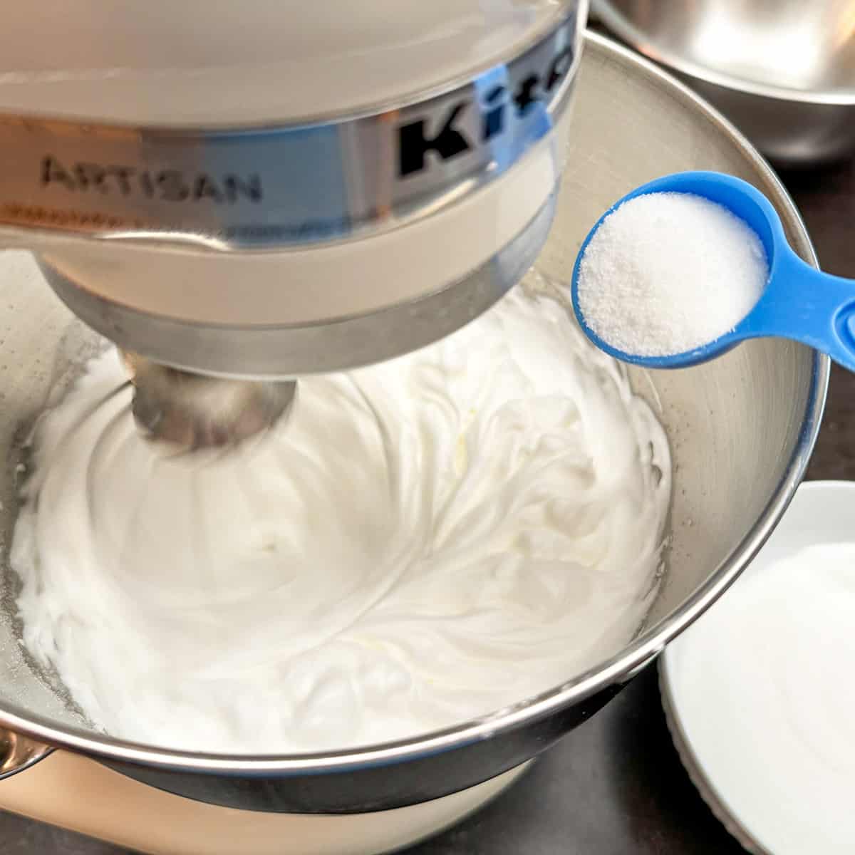 Adding sugar to a mixer that is whipping egg whites.