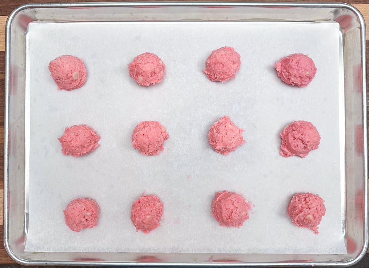 Scooped strawberry and cream cookie dough onto a parchment-lined cookie sheet pan.