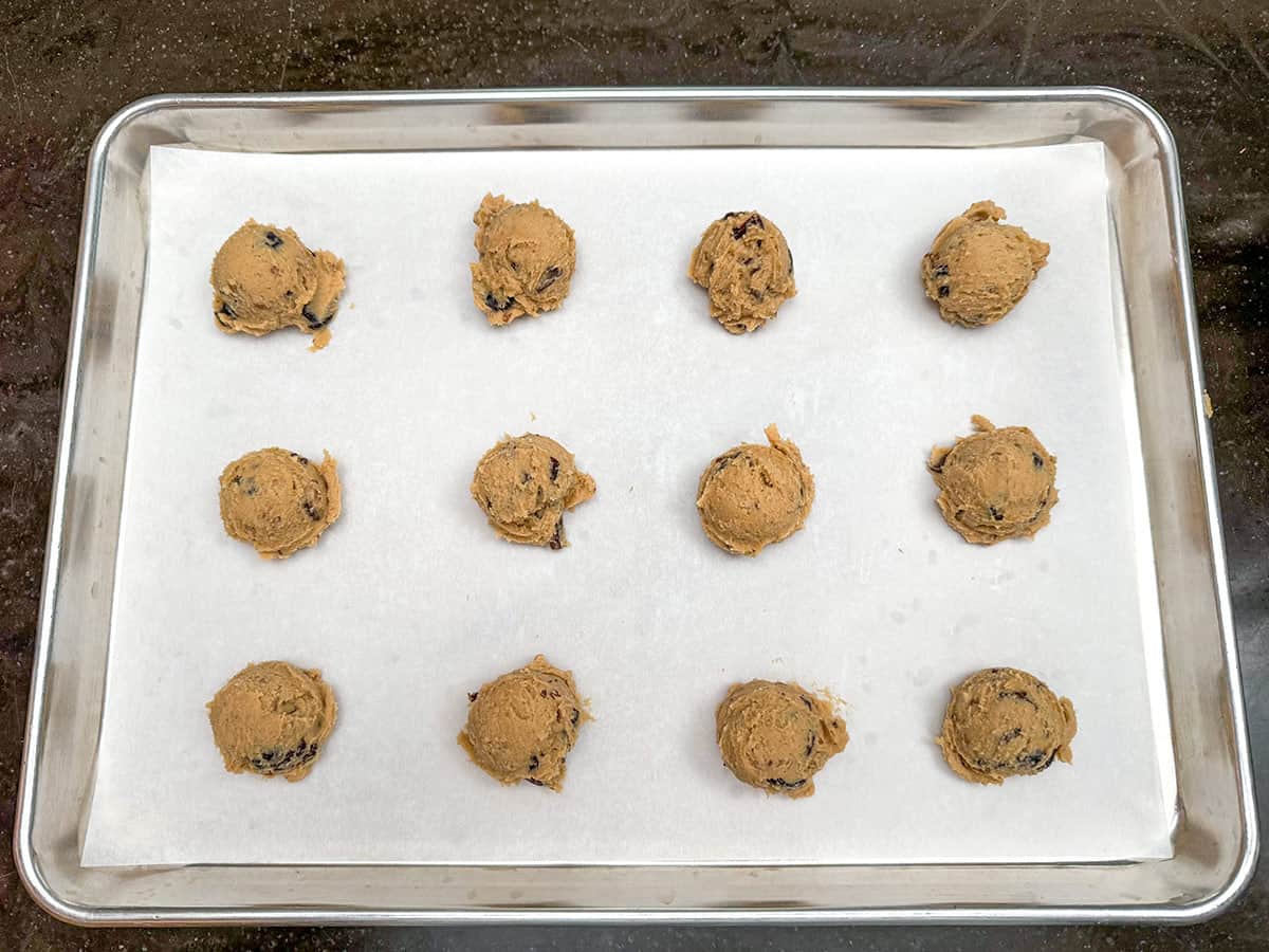 A medium scooper is used to place twelve mounds onto a parchment-lined cookie sheet pan.
