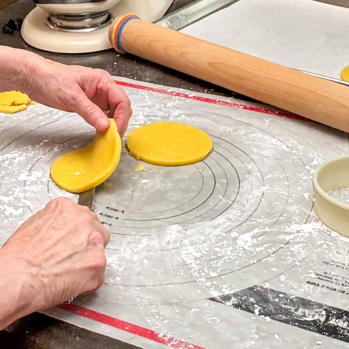 Lifting a 4-inch cutout cookie using a butter knife and your hands of a pastry mat. .