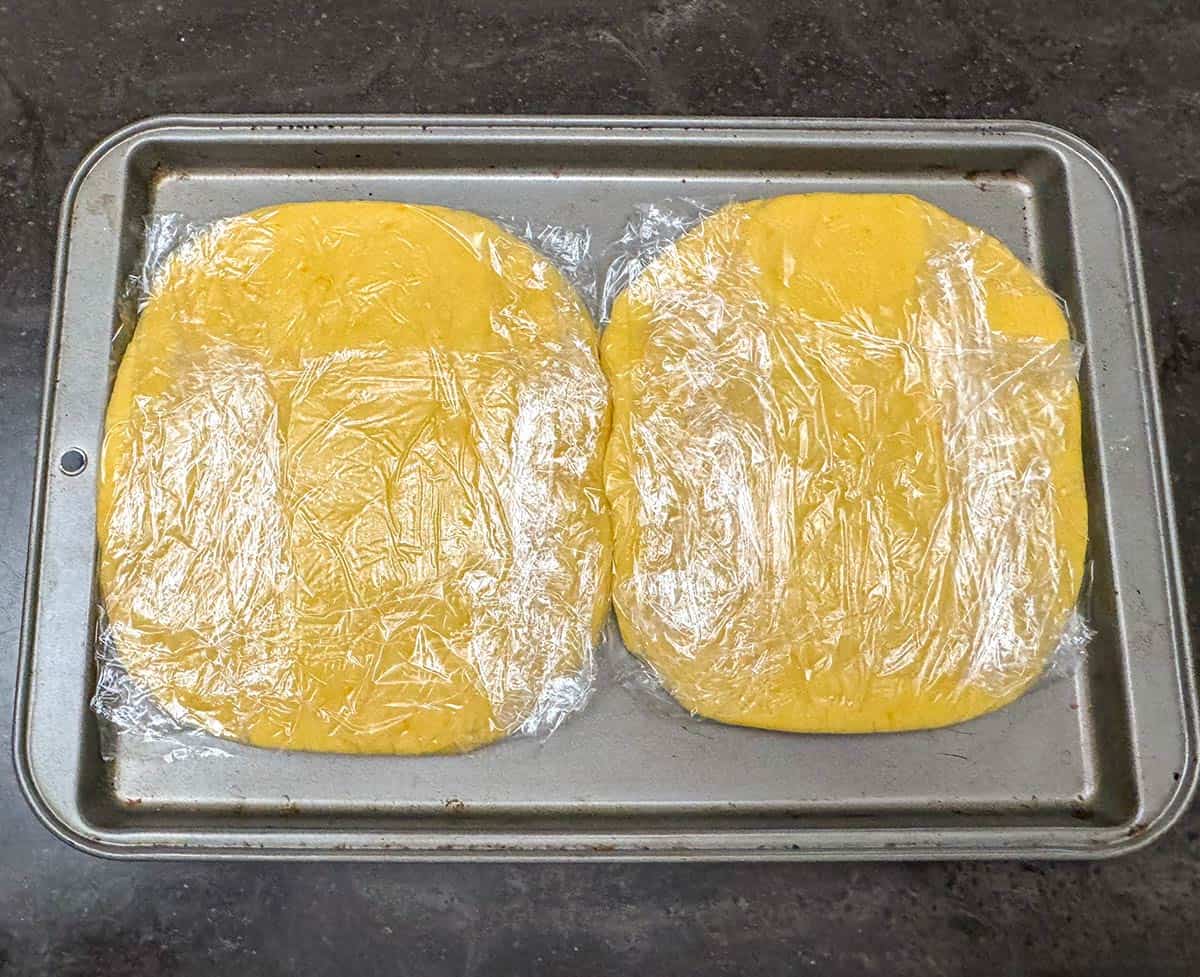 Two wrapped cookie dough on metal pan ready to be chilled.