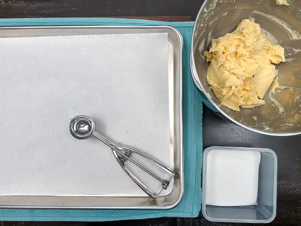 Sheet pan with parchment paper, cookie scooper, and sugar for rolling the cookie balls. Along with the cookie dough.