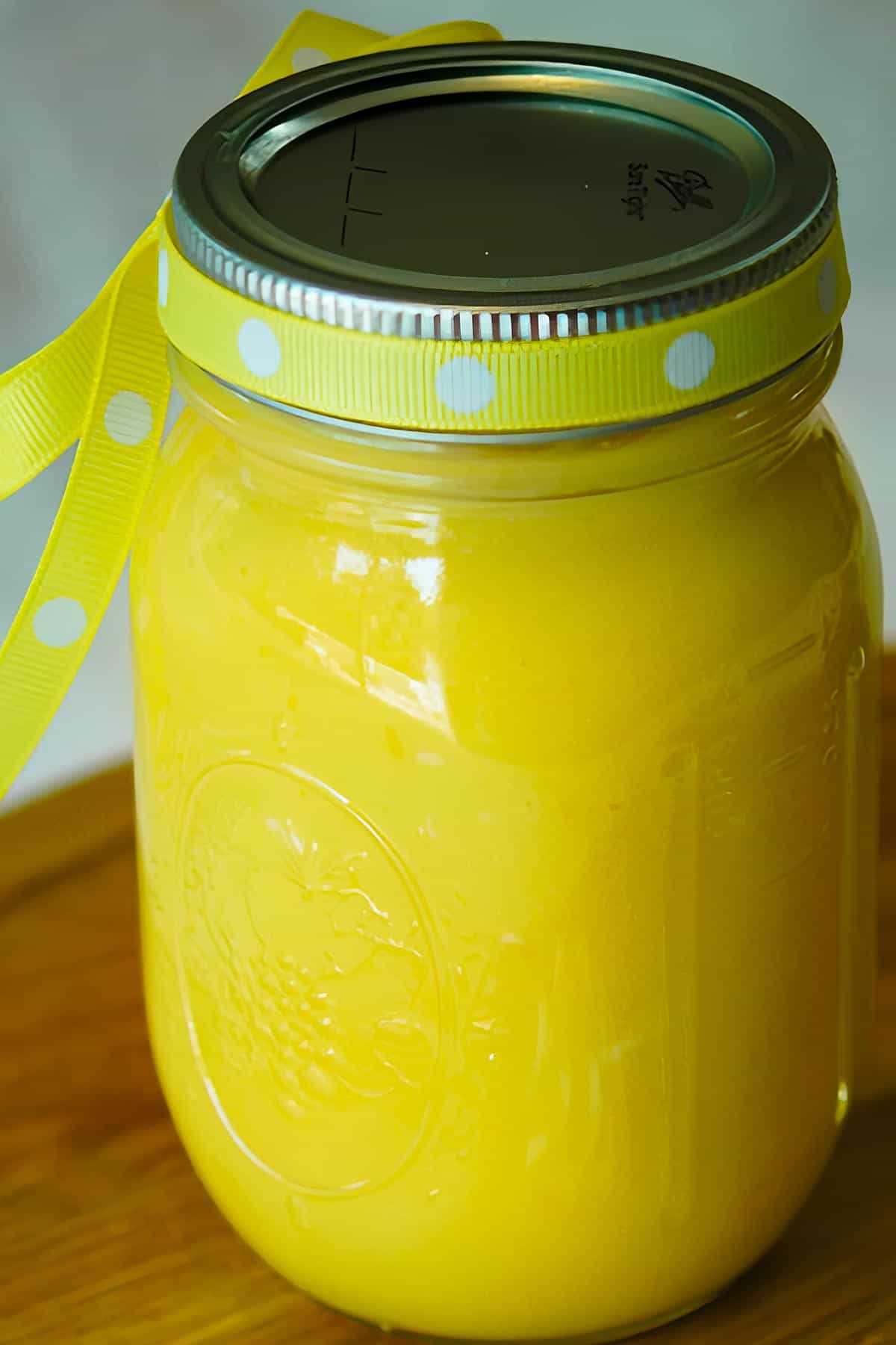 Full length of the mason jar full of lemon curd with a ribbon around the lid.