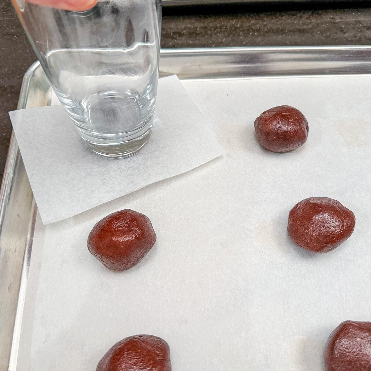 Using a square of parchment paper, place it on the round stuffed cookie, and using the bottom of a glass, press down slightly to flatten it.