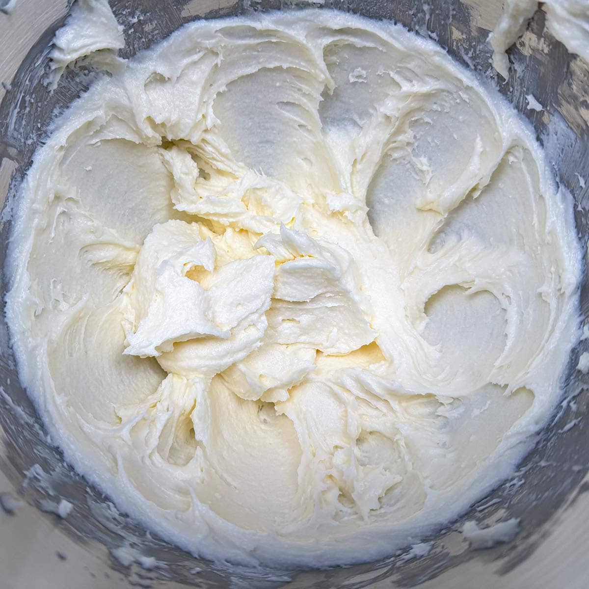 Creamy looking butter, cream cheese, and sugar, in a mixer bowl.