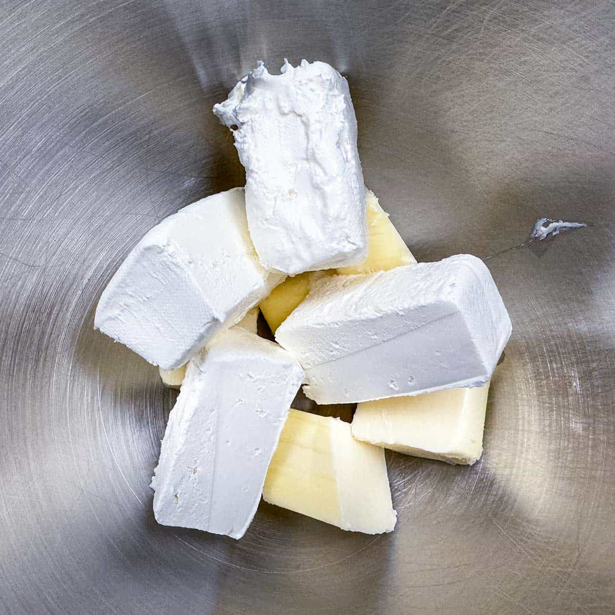 Cubed and sliced butter and cream cheese in a mixer bowl.