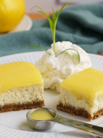 Two pieces of Lemon Cheesecake bites with Lemon Curd topping, whipped cream, and a spoonful of lemon curd.