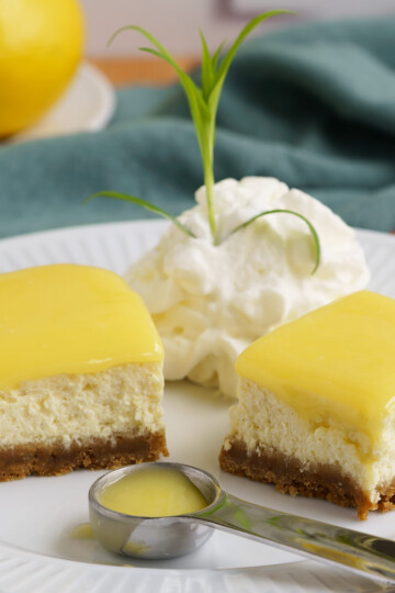 Two pieces of Lemon Cheesecake bites with Lemon Curd topping, whipped cream, and a spoonful of lemon curd.