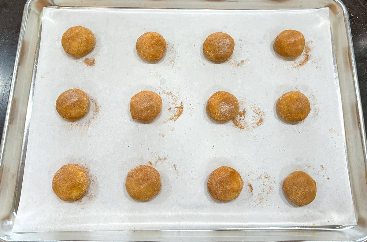 Completely covered cookie dough balls with cinnamon, cardamom, and sugar on a prepared sheet pan.