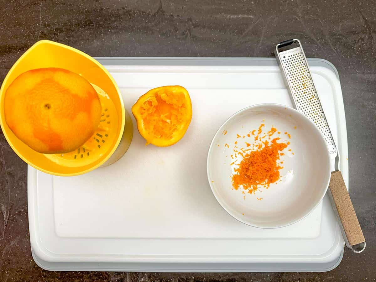An orange that is zested and then juiced on a cutting board.