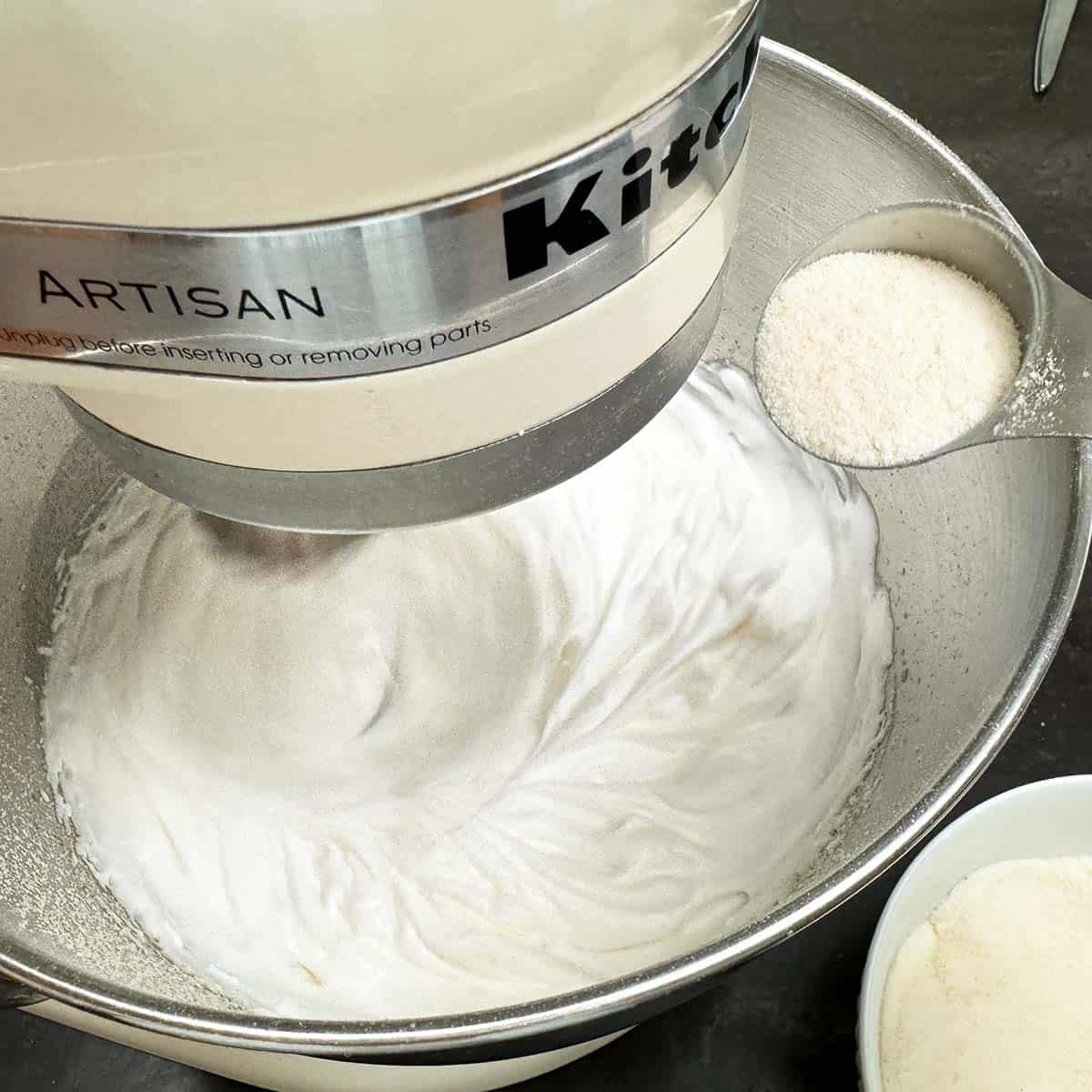Adding sugar to egg whites as they are being whipped in a mixer.