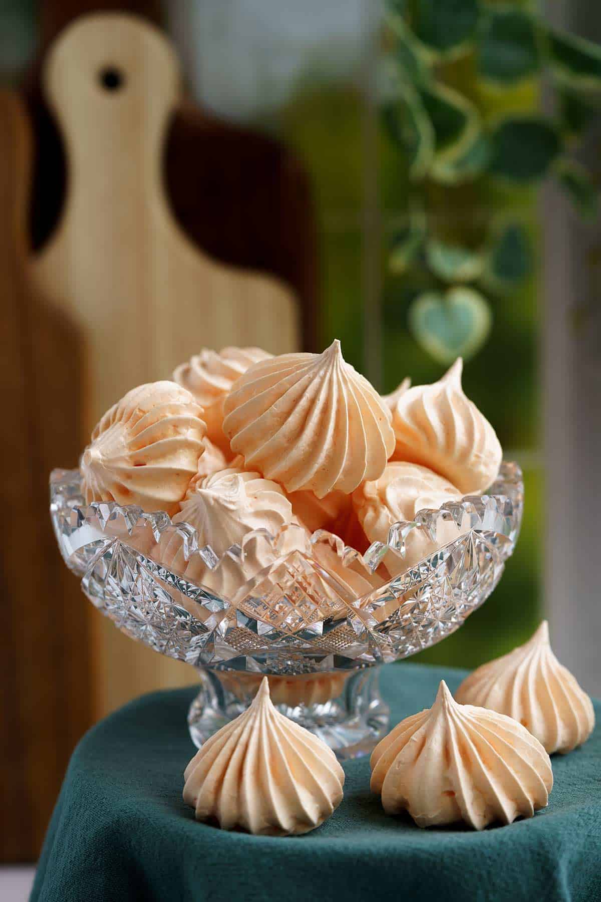 Full picture of a glass bowl with many tangerine meringue cookies inside.
