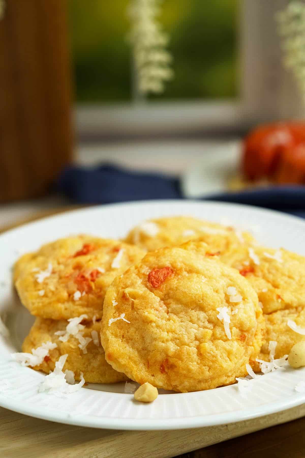 A plate full of papaya coconut and macadamia nut cookies in from of a window.