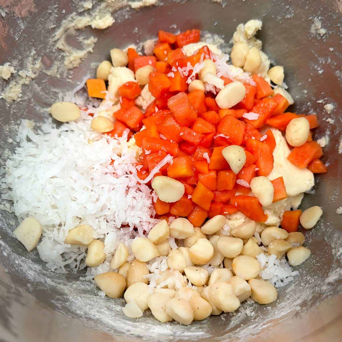 Macadamia nuts, cut-up papaya, and coconut, on top of the cookie dough in a mixer bowl.