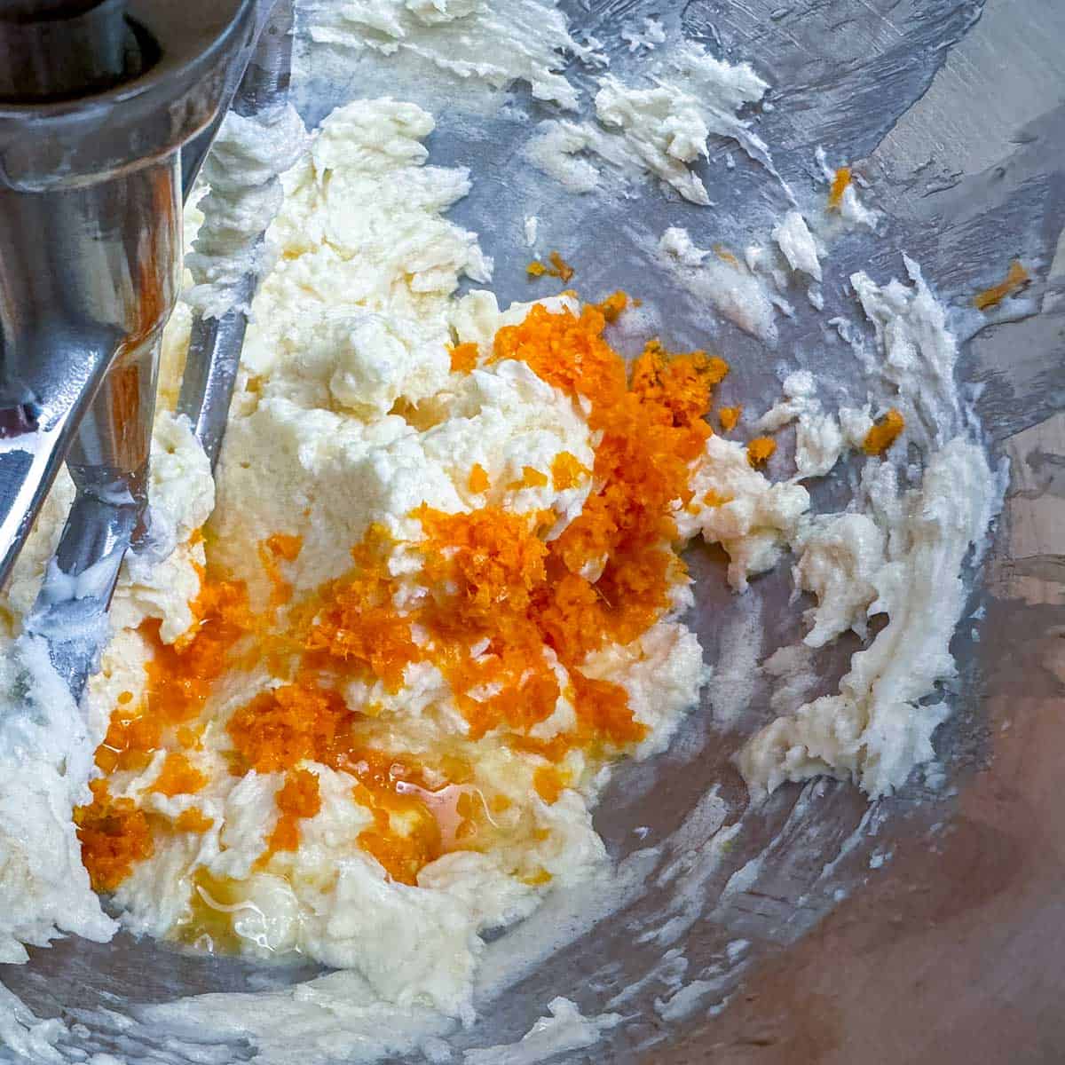 Butter sugar mixture in the bowl with orange juice and zest just getting added.