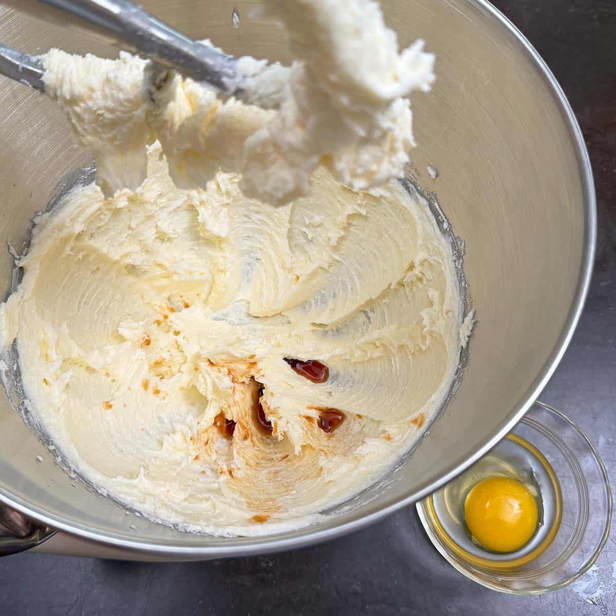 Adding vanilla extract and egg to the butter sugar mixture in a mixer bowl.