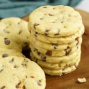 Sugar cookies with cinnamon chips and orange stacked on a wooden plank.