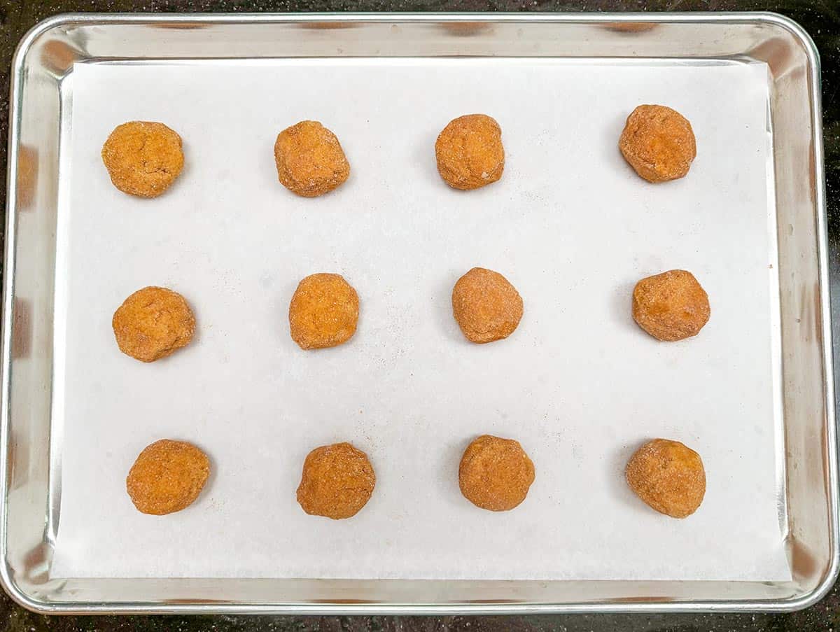 Cookie dough balls that have been rolling in the sugar-cinnamon mixture and placed on a parchment lined cookie sheet pan.