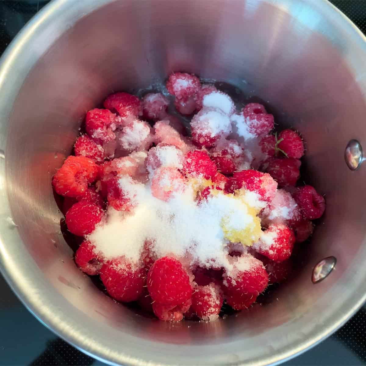 Fresh raspberries and sugar along with the lemon zest added to a saucepan.