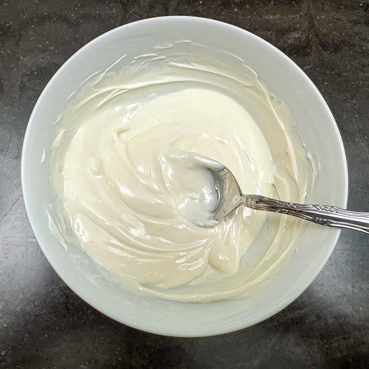 A bowl of melted white chocolate wafer that is smooth and able to be stirred.