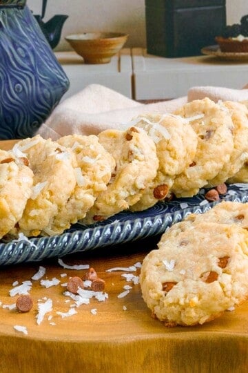 Cinnamon chips with coconut and almonds cookies lined up on a narrow dish with a few on the wooden block.