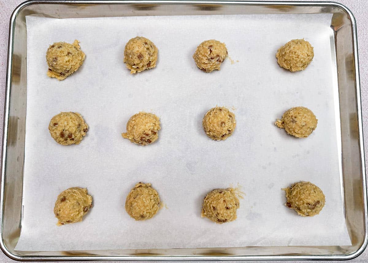 Scooped cookie dough on a parchment paper lined cookie sheet pan.