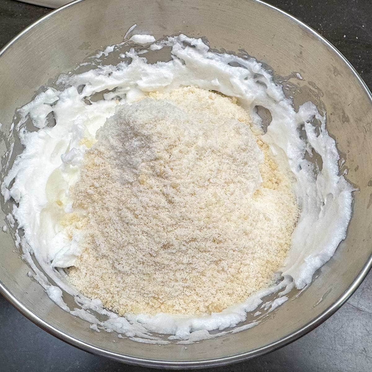 Almond mixture being folded into beaten egg whites.