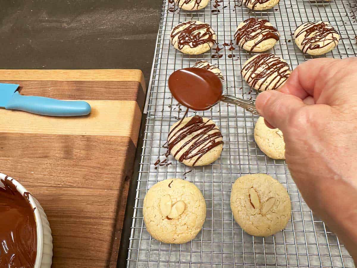 Using a spoon to drizzle melted chocolate over cooled cookies.