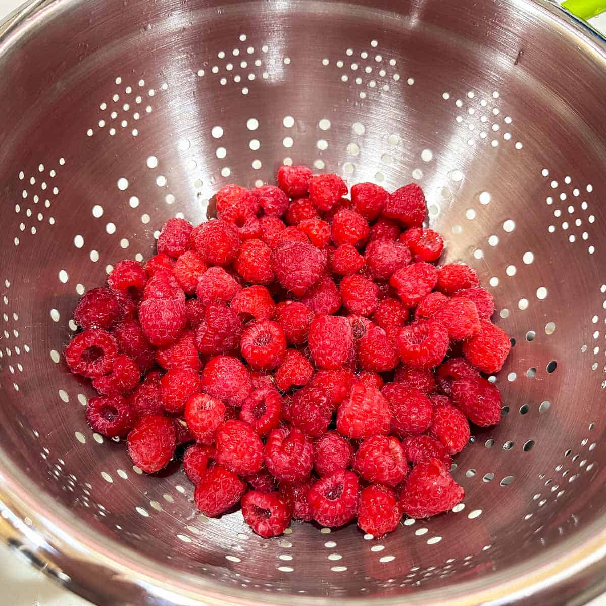 Fresh raspberries in a strainer getting washed.