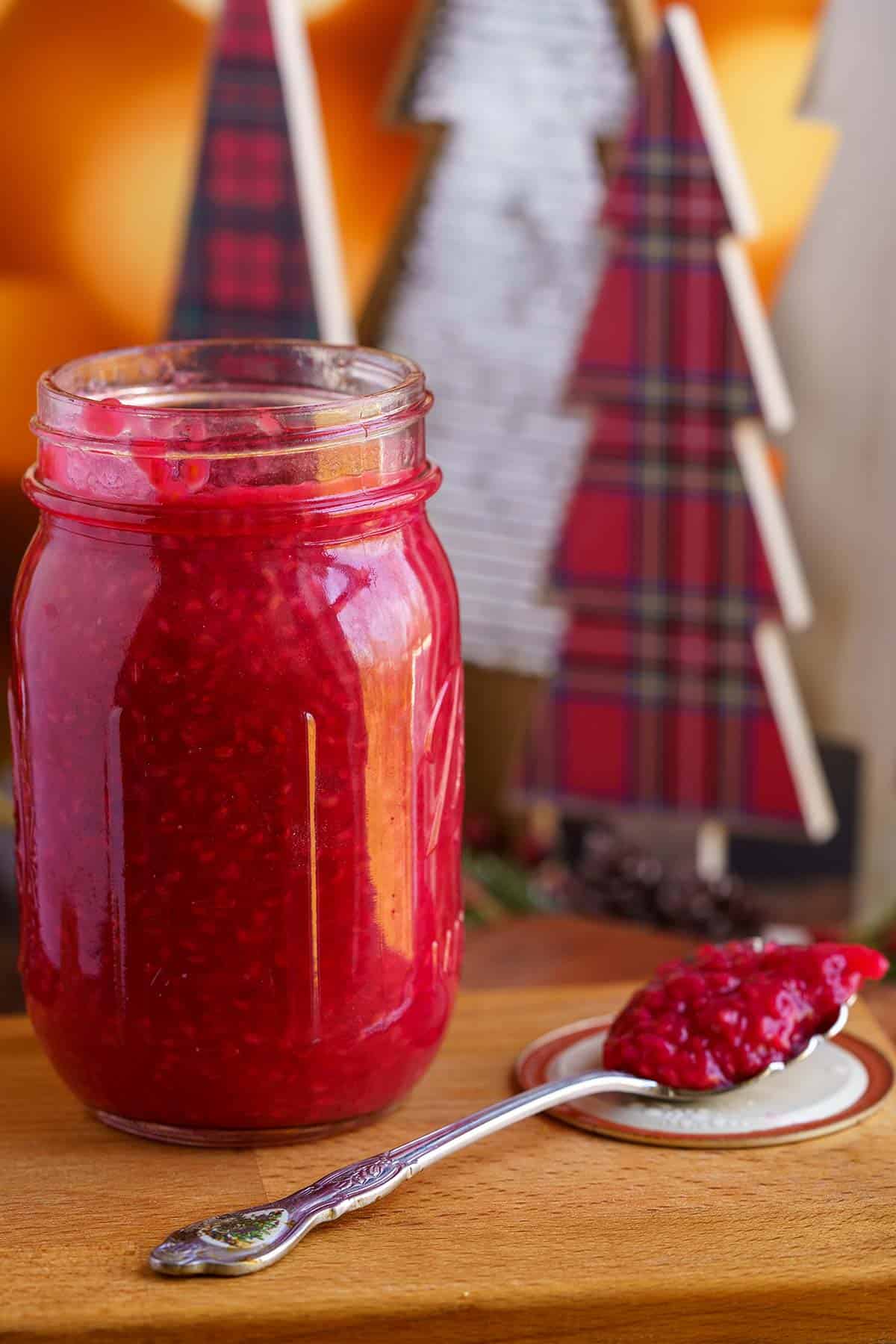 Raspberry filling in a glass jar and a spoonful sitting right next to the jar.