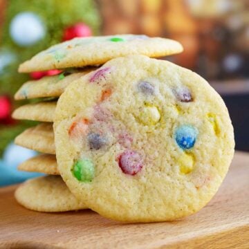 Mini M&M cookies on a wooden board with a stack if the cookie and one leaning against it for the front view.