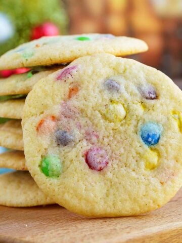 Mini M&M cookies on a wooden board with a stack if the cookie and one leaning against it for the front view.