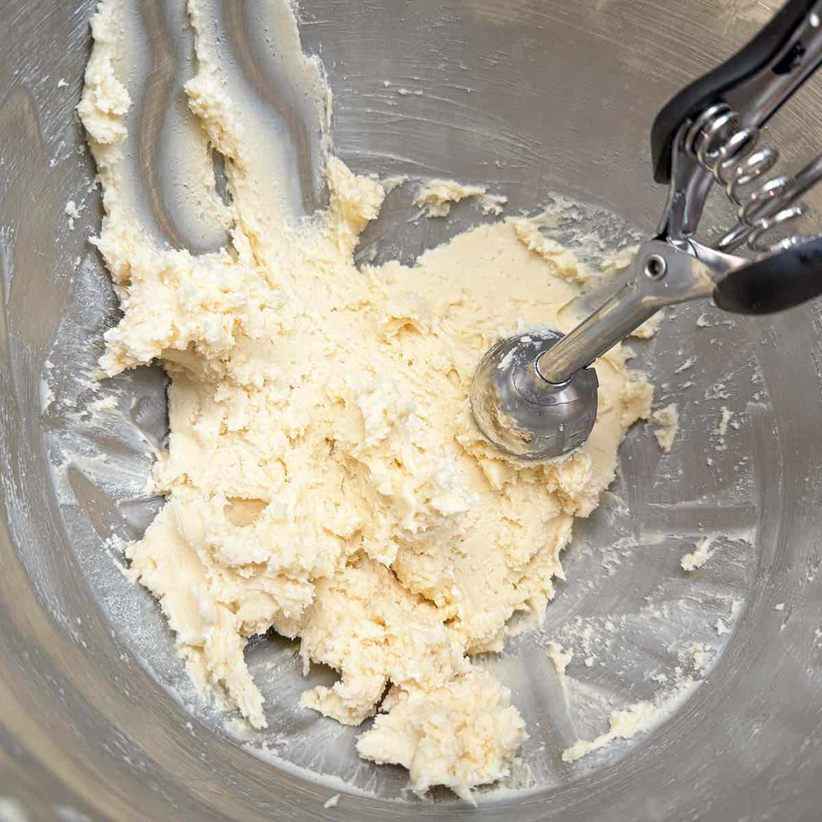 Cookie scooper sitting in the completed cookie dough in a mixer bowl.