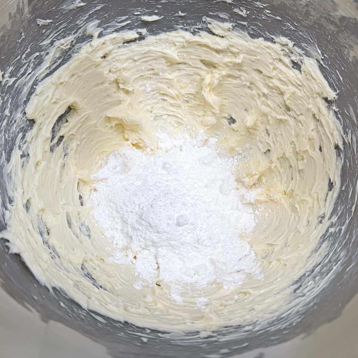 Adding powdered sugar to the creamed butter in a mixer bowl.