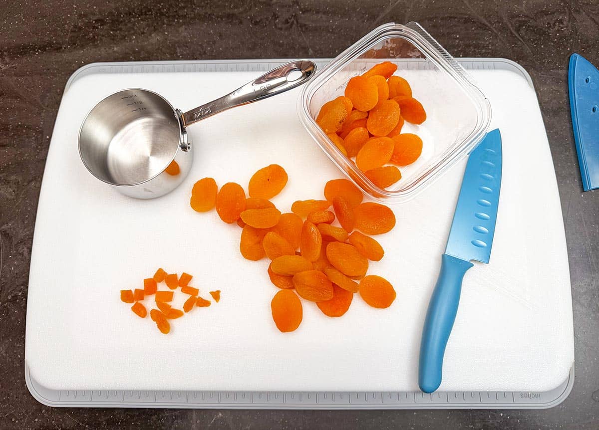 Cutting up dried apricots on a cutting board with a sharp knife.