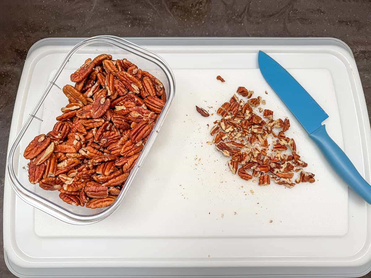 Chopping pecans on a cutting board with a sharp knife.