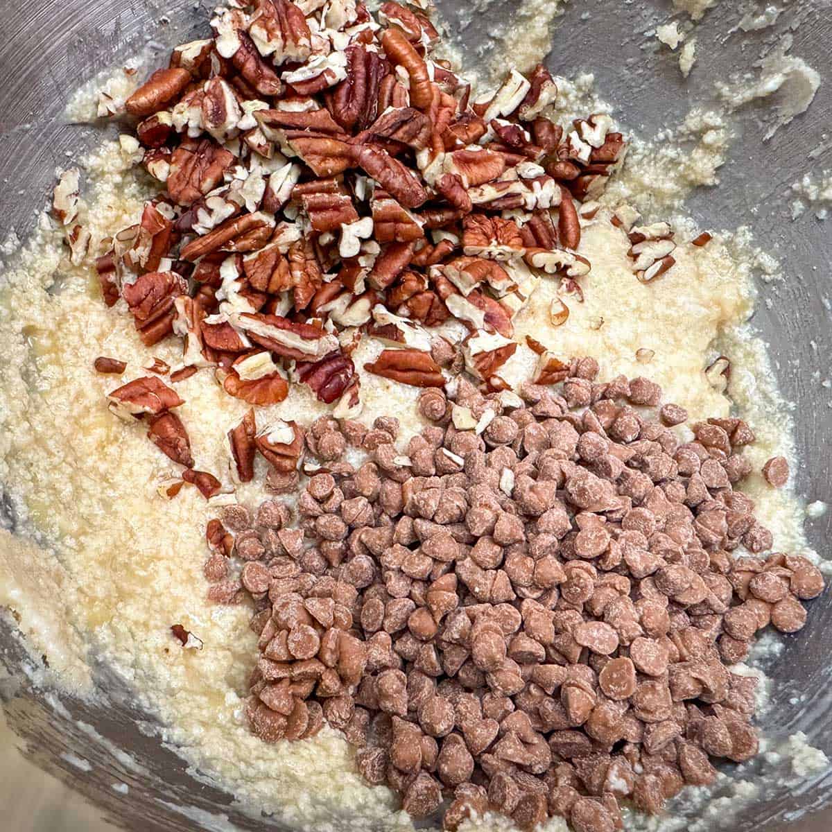 Adding the caramel chips and the chopped pecans to the wet cookie dough mix.