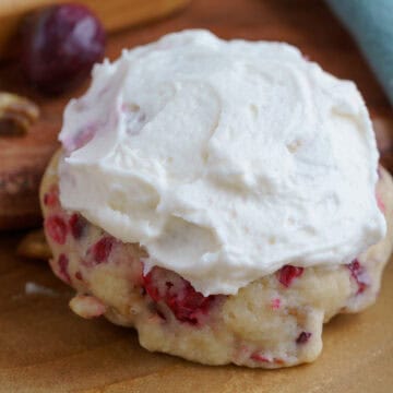 A fresh cranberry and walnut frosted cookie on a wooden plank.