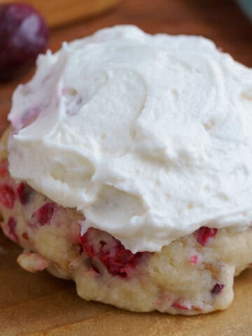 A fresh cranberry and walnut frosted cookie on a wooden plank.