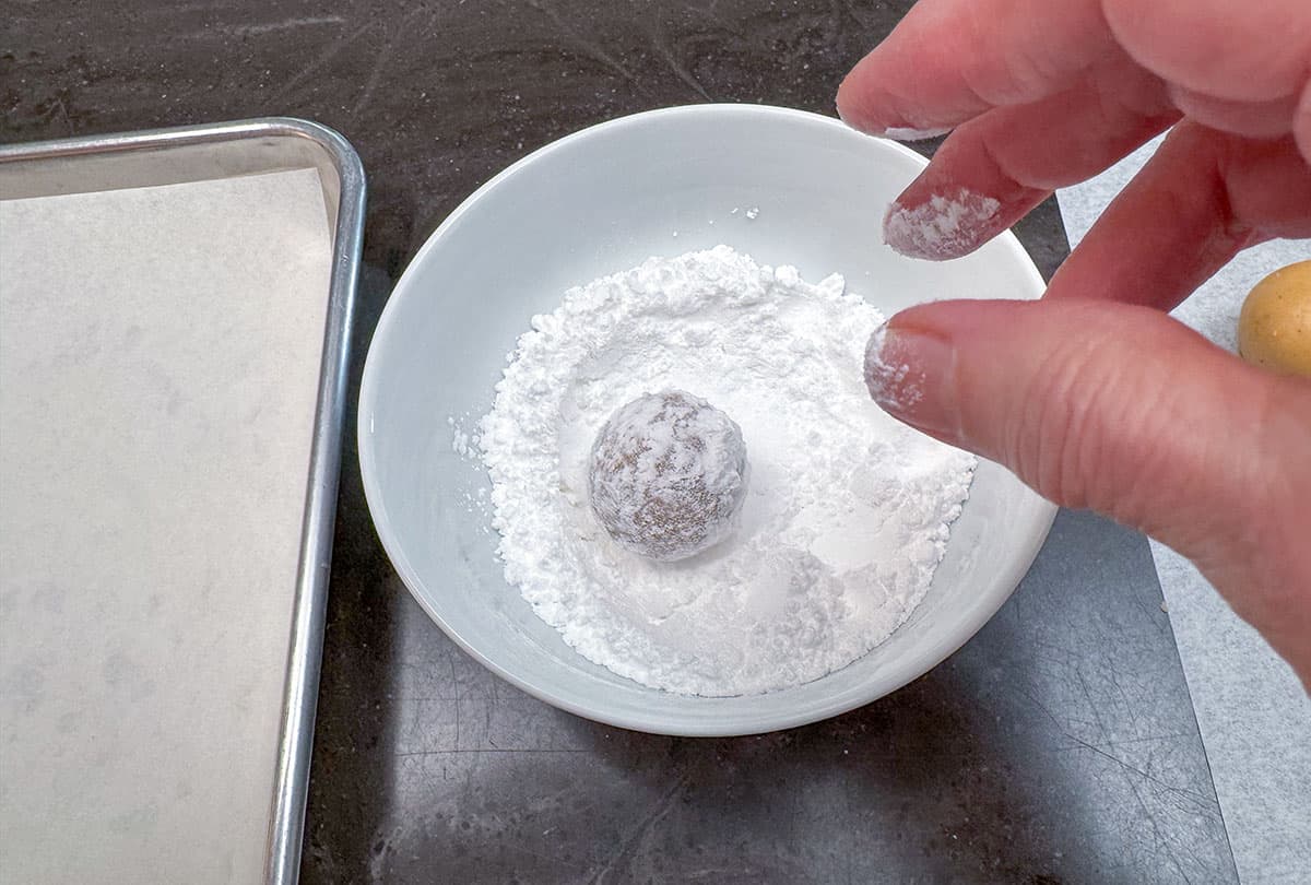 Rolling and coating the cookie balls in powdered sugar.