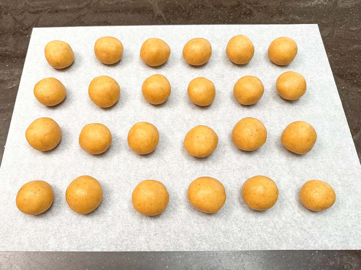 Cookie balls that are on a piece of parchment paper.