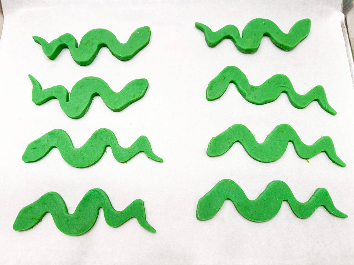 Eight snake cutout cookies on a sheet pan and ready to be baked.