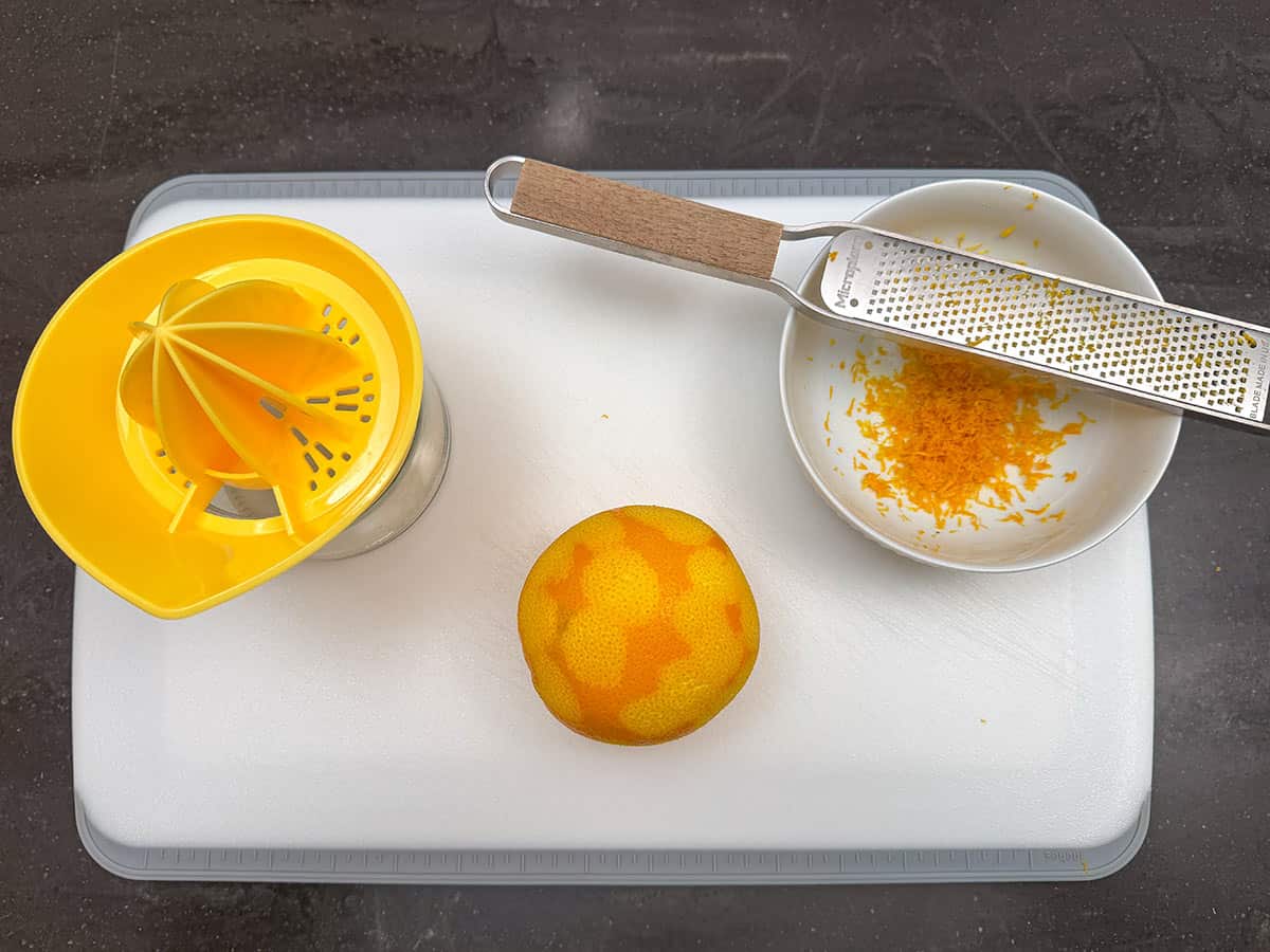 Cutting board with orange. Also, juicer and zester with bowl.