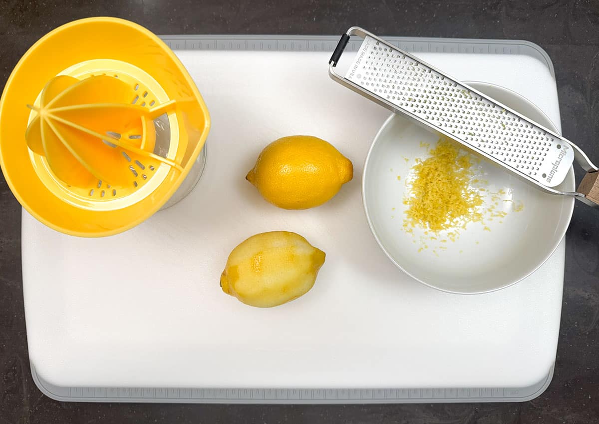 Lemons on a cutting board being juiced and zested.