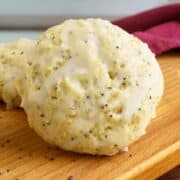 Lemon poppy seed cookies on a wooden board with poppy seeds all around.